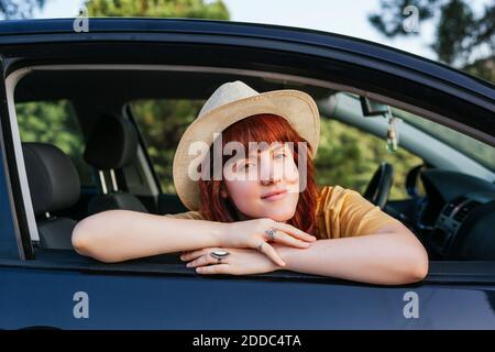 Sorridente giovane bella donna rossa che si appoggia fuori dal finestrino dell'auto Foto Stock