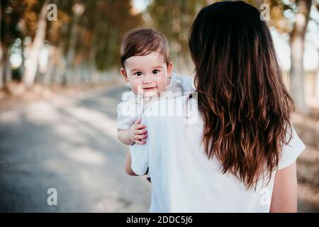 Madre che trasporta il bambino mentre si sta sulla strada all'aperto Foto Stock