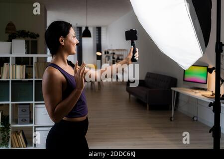 Giovane donna che fa cinque alti mentre la registrazione video davanti di riflettori a casa Foto Stock