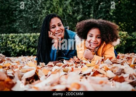 Donna e ragazza sorridenti con la testa in mano sdraiata foglie caduto al parco Foto Stock