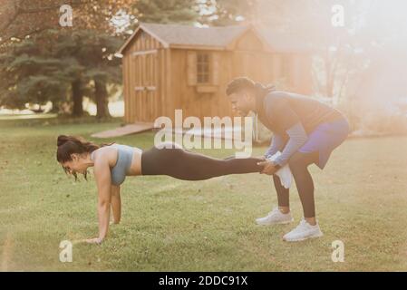Uomo che tiene le gambe della donna mentre si esercita in cortile Foto Stock