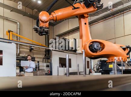 Giovane uomo d'affari con il laptop che esamina la macchina automatica del braccio del robot a. fabbrica Foto Stock