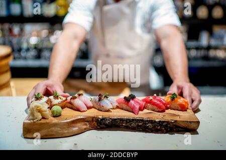 Chef maschile con sushi su vassoio di servizio in legno in cucina al ristorante Foto Stock