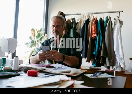 Uomo Costume designer utilizzando smartphone mentre si lavora al tavolo in studio Foto Stock