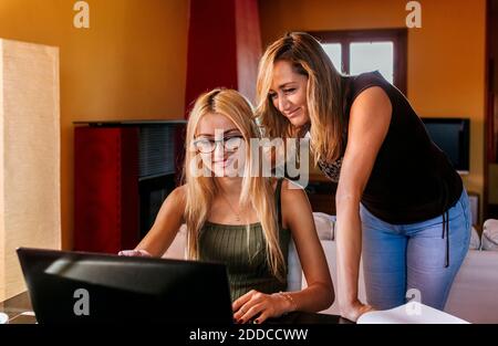 Madre che guarda il portatile mentre figlia fa i suoi studi in linea a casa Foto Stock