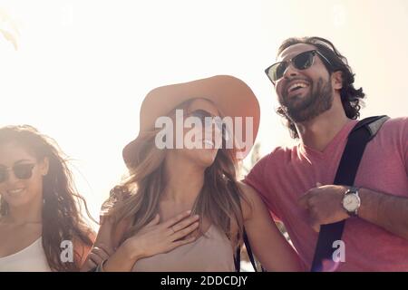 Sorridendo amici maschili e femminili in occhiali da sole che parlano contro chiaro cielo Foto Stock