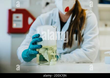 Giovane donna che tiene evaporare il bicchiere liquido di fumo mentre si sta a. laboratorio Foto Stock