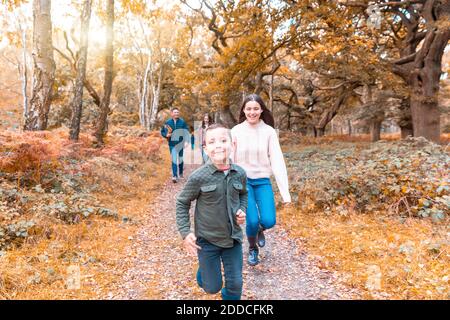 Fratello e sorella corrono felicemente mentre i genitori camminano dietro dentro Parco Cannock Chase in autunno Foto Stock