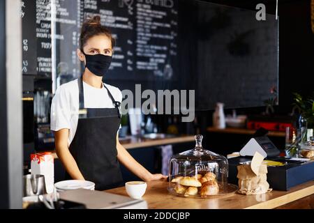 Ritratto della cameriera che indossa una maschera protettiva mentre si lavora caffetteria Foto Stock