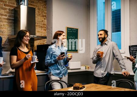 Sorridente imprenditori maschili e femminili che discutono mentre hanno caffè dentro cucina sul posto di lavoro Foto Stock