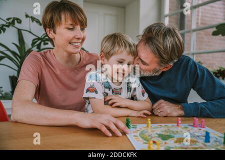 Padre nuzzling figlio mentre la madre si siede accanto a giocare gioco da tavolo a casa Foto Stock