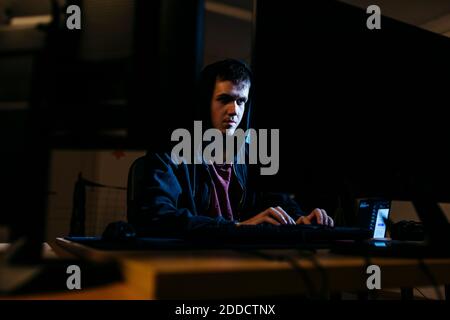 Giovane hacker che lavora al computer mentre si siede in ufficio Foto Stock