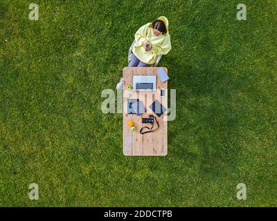 Vista aerea della donna seduta al tavolino da caffè prato verde con tazza di caffè in mano Foto Stock