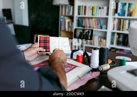 Maschio su misura che spiega circa tessuto attraverso vlogging sul telefono mobile in studio Foto Stock