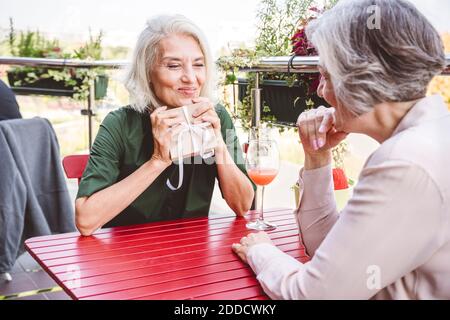 Donna felice che tiene il regalo mentre sedendo con l'amico femmina a. ristorante Foto Stock