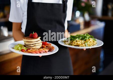 Sezione centrale del barista femminile che tiene la piastra di cibo in una caffetteria Foto Stock