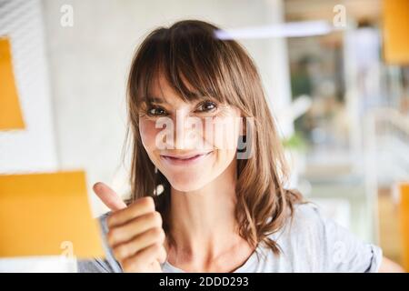 Donna matura che gesturing mentre guardando le note appiccicose si attaccano sopra materiale in vetro Foto Stock