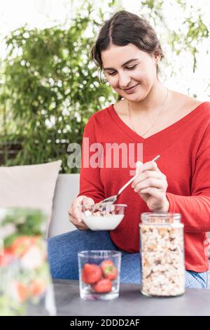 Donna sorridente che tiene la preparazione della farina d'avena mentre si siede in cortile Foto Stock