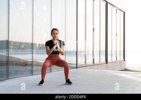 Giovane sportivo che fa esercizio di squadra sulla passeggiata contro la finestra di vetro Foto Stock