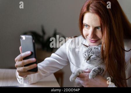 Giovane donna che prende selfie smartphone con gatto sul giro Foto Stock