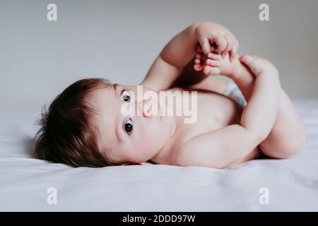Il bambino tocca le gambe mentre si sdraiava sul letto Foto Stock