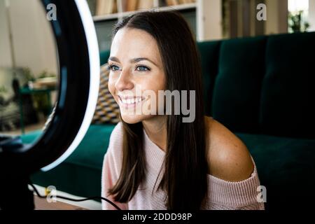 Sorridente bella vlogger femminile con illuminazione attrezzature a casa Foto Stock