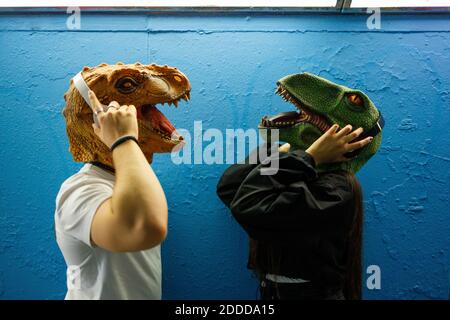 Amici di sesso maschile e femminile che ascoltano la musica con le cuffie mentre indossare una maschera di dinosauro contro la parete blu Foto Stock