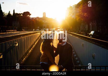 Coppia che si guarda l'un l'altro mentre si siede su ringhiera ponte in città durante il tramonto Foto Stock