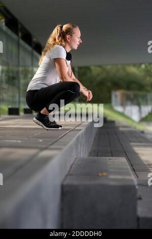 Atleta con cuffie intorno al collo che si accovacciano sul sentiero Foto Stock