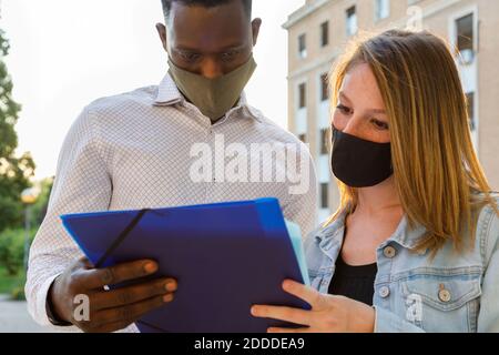 Studenti universitari maschi e femmine che indossano maschera protettiva mentre discutere nel campus Foto Stock