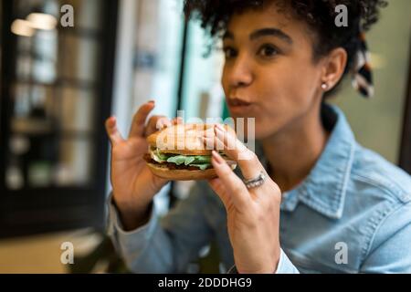 Donna di mezza età adulta che mangia hamburger mentre si siede al bar Foto Stock