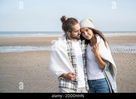 Giovane coppia coperta di coperta che passa il tempo libero in spiaggia durante il fine settimana Foto Stock