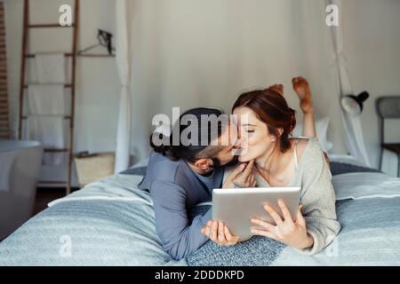 Uomo che baciava la donna mentre usa il tablet digitale a casa Foto Stock