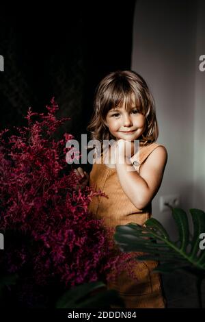 Ragazza sorridente con la mano nel mento in piedi a casa Foto Stock