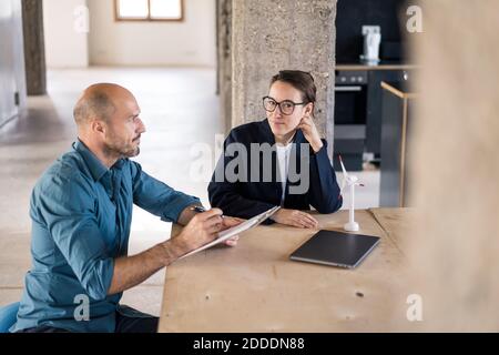 Uomo d'affari con il pad di nota che guarda la donna premurosa mentre si siede in ufficio Foto Stock