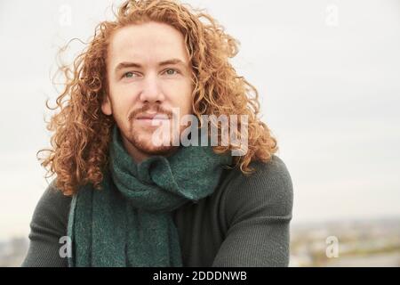 Contemplando l'uomo lungo dei capelli che guarda via contro il cielo Foto Stock