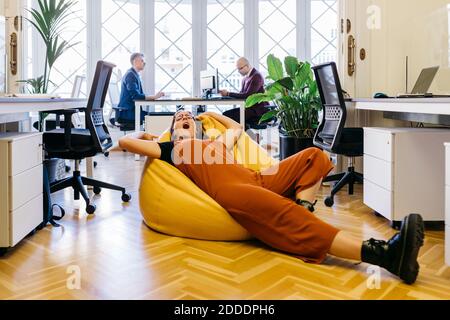 Donna d'affari esausta che riposa sul sacchetto del fagiolo in ufficio Foto Stock