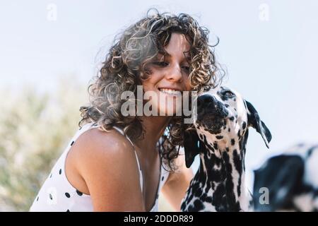 Giovane donna sorridente con cane dalmata durante il giorno di sole Foto Stock