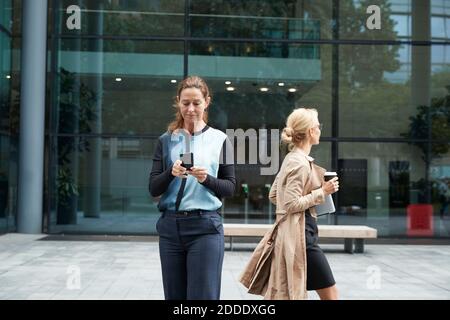 Donna d'affari che usa il telefono cellulare con un collega che lascia dopo il lavoro dentro sfondo Foto Stock