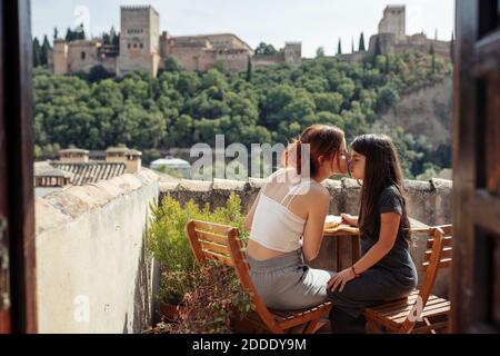 Madre e figlia si baciano mentre si siedono sul tavolo sulla terrazza Foto Stock