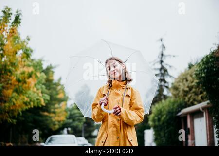 Sorridente ragazza in impermeabile che tiene l'ombrello mentre si trova in città Foto Stock