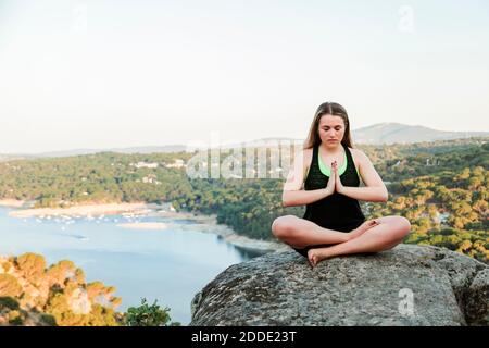 Bella donna meditando sulla roccia sulla montagna contro il cielo limpido Foto Stock