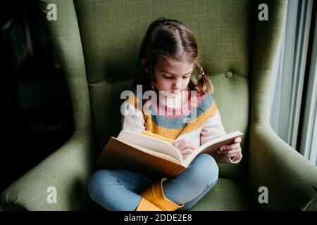Ragazza cute che scrive nel libro mentre sedendo sulla sedia a. casa Foto Stock