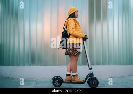 Donna matura che guida scooter elettrico a spinta sul sentiero a parete Foto Stock