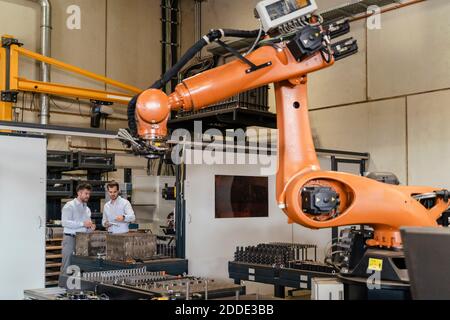 Macchina automatica con braccio robotico con uomini d'affari in piedi sullo sfondo a. fabbrica Foto Stock