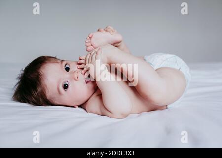 Cute bambino ragazzo che mette il piede in bocca mentre si sdraiava sopra letto a casa Foto Stock