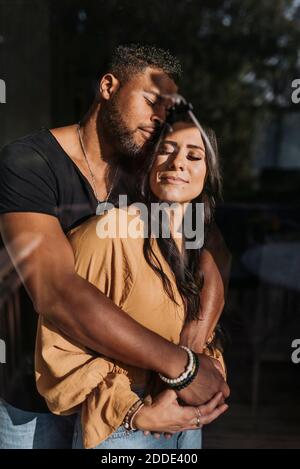 Uomo che abbraccia la donna in piedi con gli occhi chiusi a casa Foto Stock