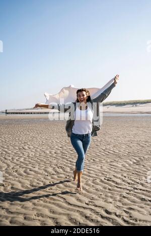 Donna allegra che corre mentre tiene coperta alla spiaggia durante il fine settimana Foto Stock