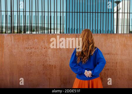 Donna rossa in piedi con le mani dietro di fronte parete marrone Foto Stock