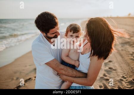 Madre e padre abbracciano il figlio mentre si è in piedi in spiaggia durante tramonto